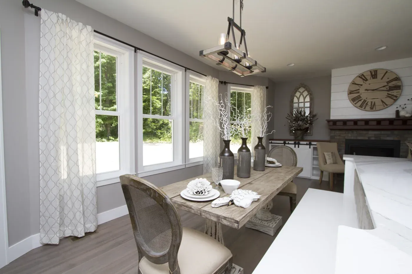 Modern farmhouse dining room with wood table, patterned curtains, pendant lighting, fireplace with clock, and open-concept kitchen visible on right