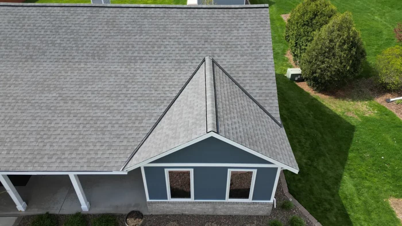 Aerial view of a blue home with a newly installed gray asphalt shingle roof and front gable.