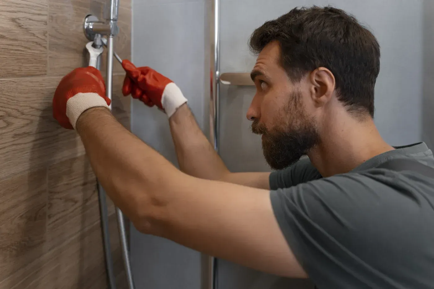 Technician installing or adjusting a shower fixture on a tiled bathroom wall during a bath remodeling project.