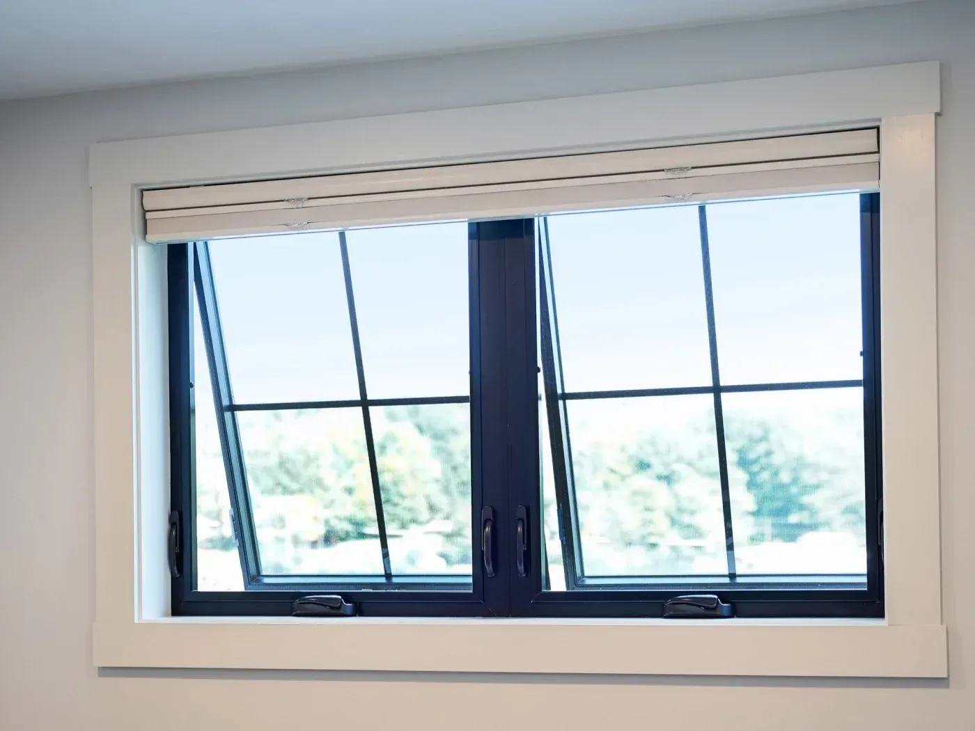 Large modern window with dark frames and horizontal muntins, partially open, showing outdoor landscape view with trees and sky