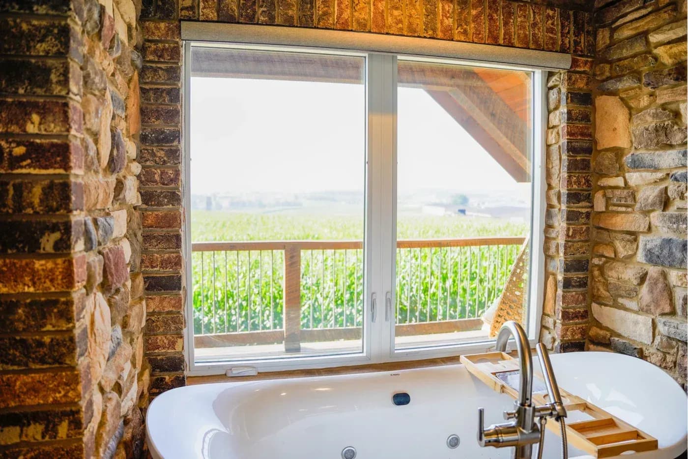Bathroom with soaking tub and faucet facing sliding glass doors overlooking a cornfield and rural landscape