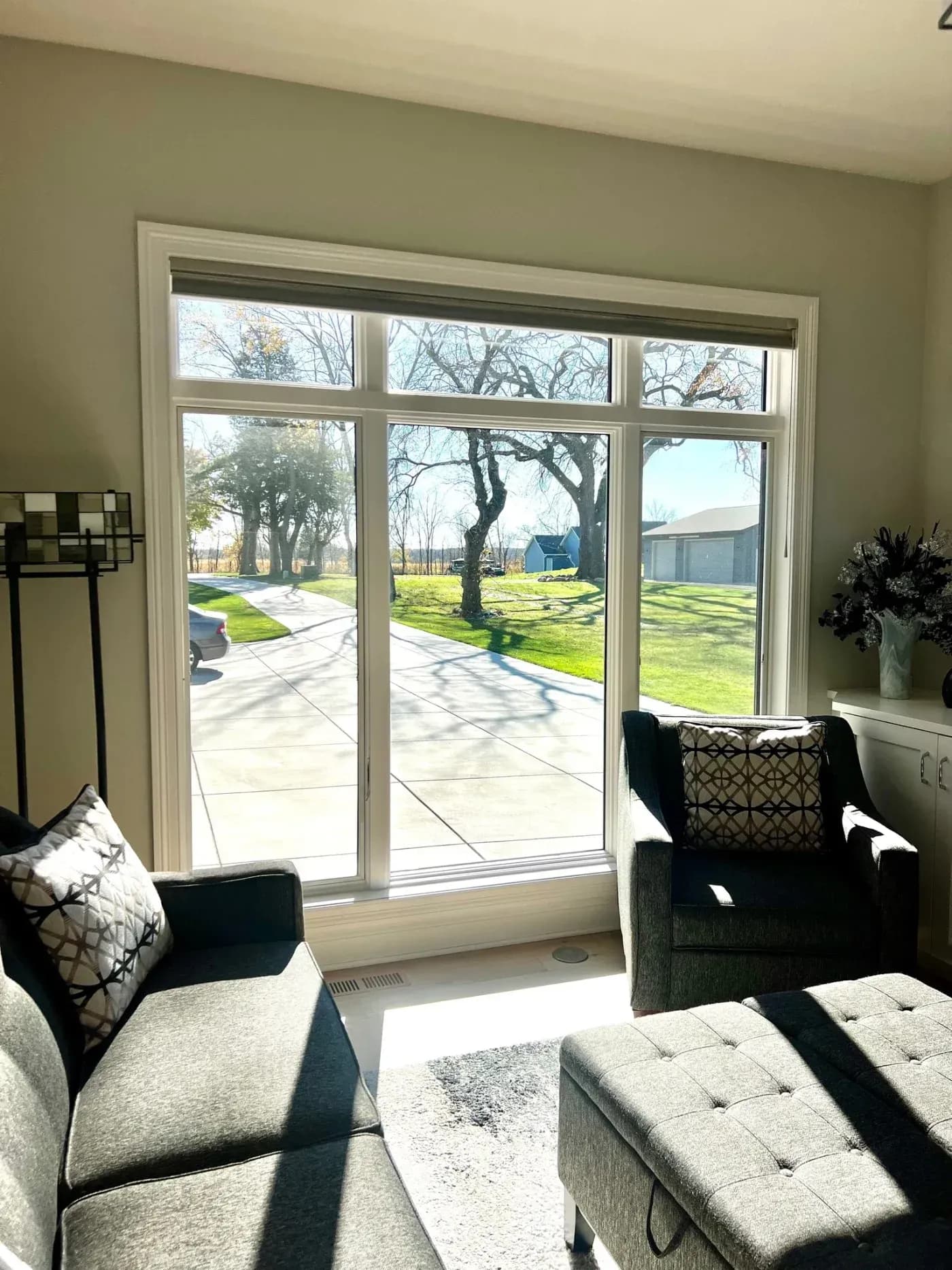 Living room with large sliding glass doors opening to patio, lawn with mature trees, and neighborhood houses visible outside