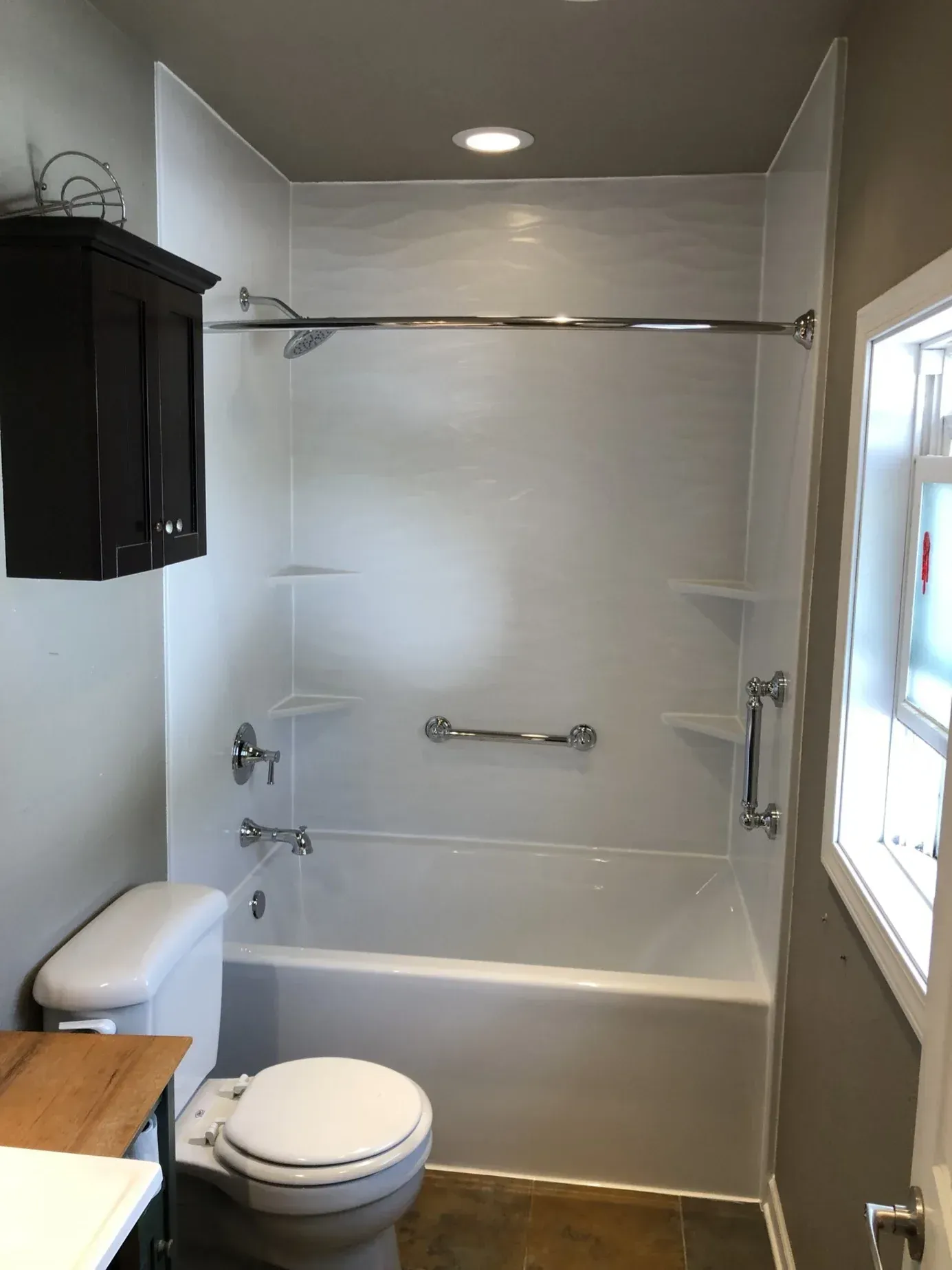 Modern bathroom with white fiberglass shower-tub combo, chrome fixtures, recessed lighting, two toilets, black cabinet, and window