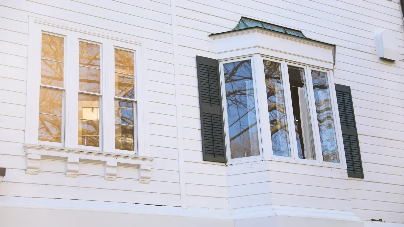 White home exterior featuring tall multi-pane windows and a projecting bay window with black shutters.