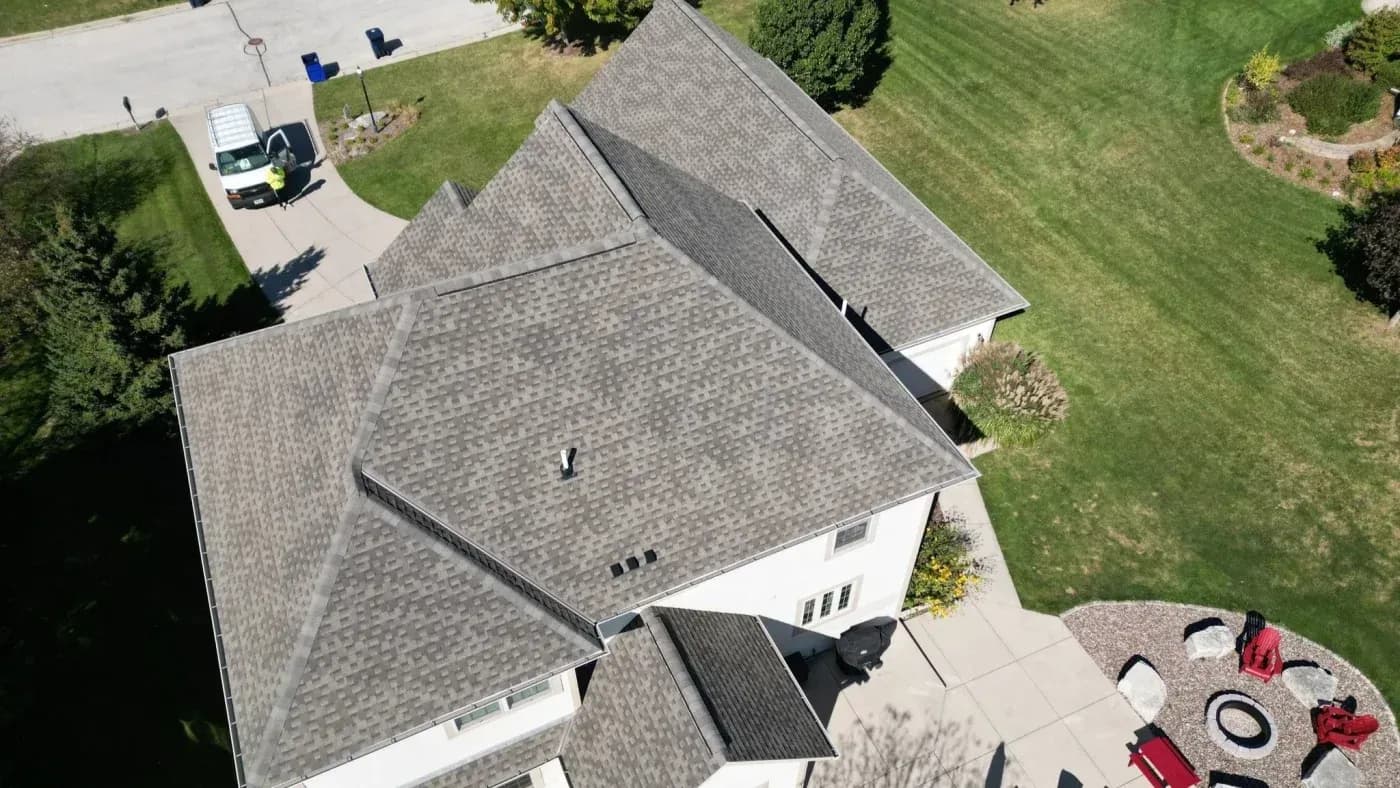 Drone view of a large residential home with a multi-section gray shingle roof and landscaped backyard.