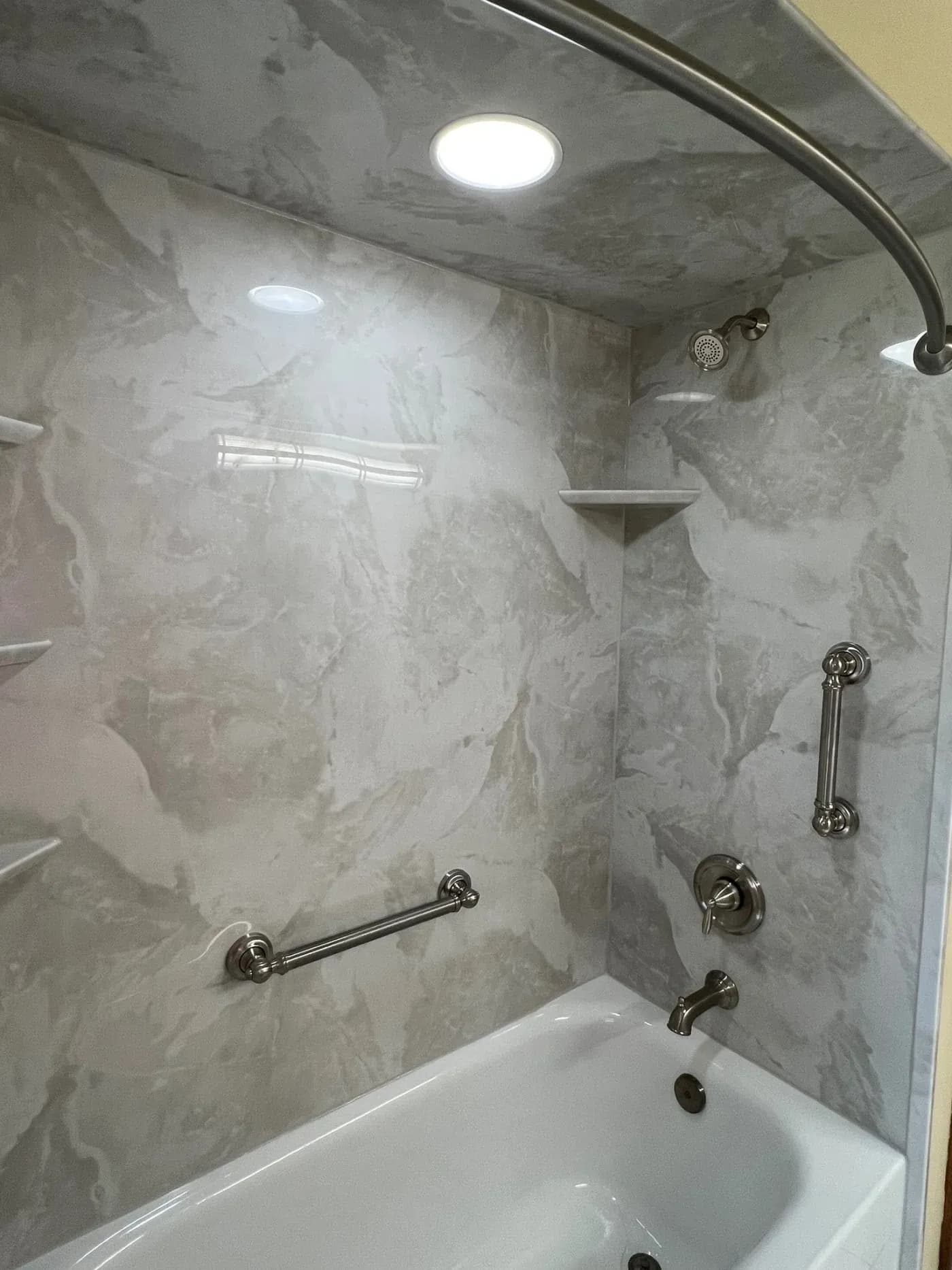 Modern marble shower enclosure with white bathtub, chrome fixtures, grab bars, showerhead, and recessed ceiling lights