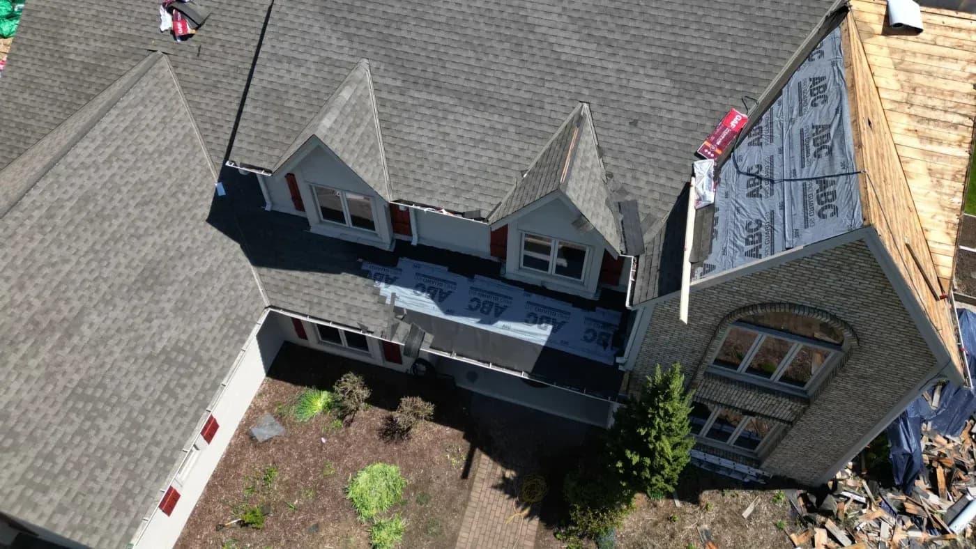 Aerial view of residential homes under construction with protective roofing, new shingle installation, and landscaping in progress