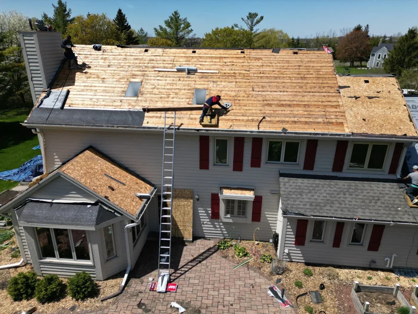 Roofer in red jacket installing wooden shingles on residential house roof during renovation project
