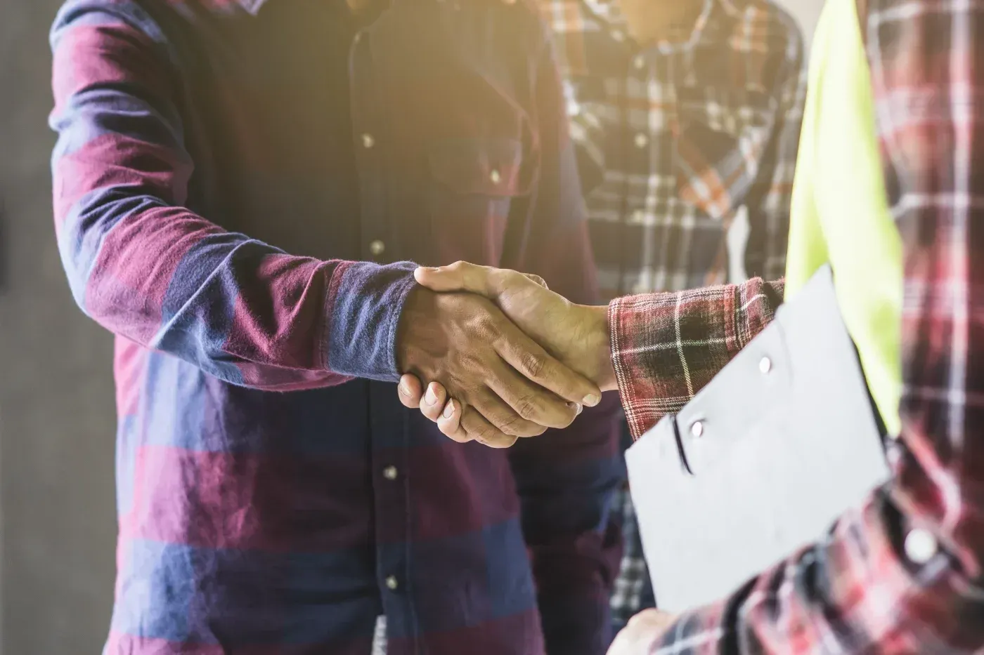 Two workers in plaid shirts shaking hands in agreement or greeting at a construction or industrial site