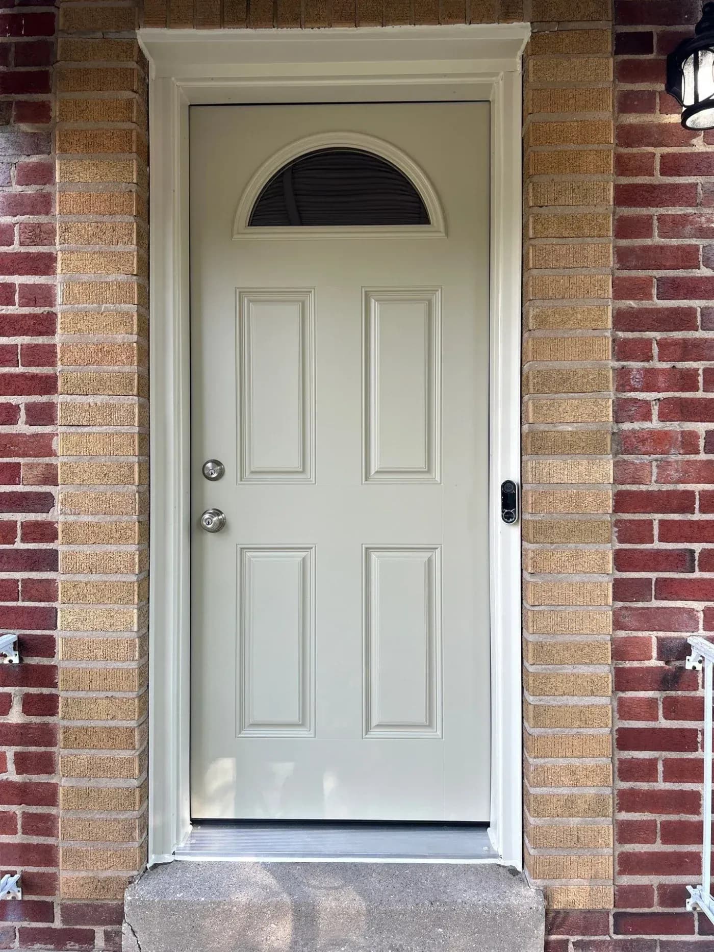 Cream-colored front door with six raised panels and arched transom window set in red brick entryway with white frame trim