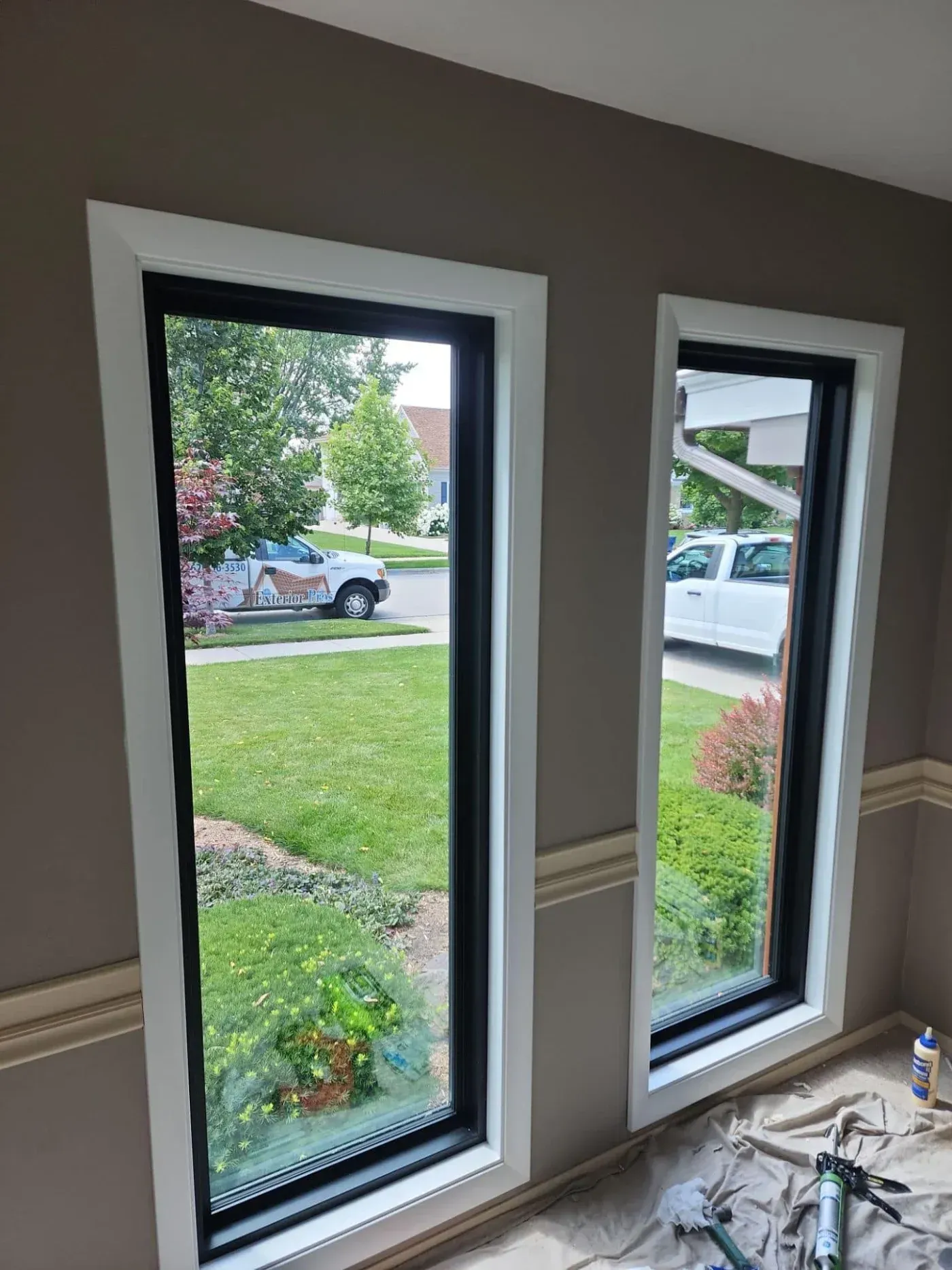 Two newly installed patio doors with white frames and black glass, looking out onto a residential yard with lawn, landscaping, and parked vehicles