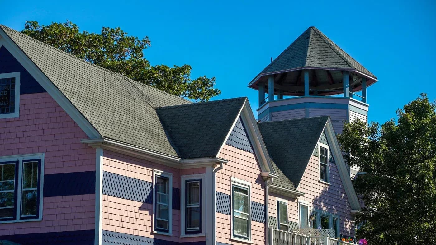 Coastal Victorian homes with pink and white shingle siding, peaked roofs, and a distinctive cupola tower under clear blue sky