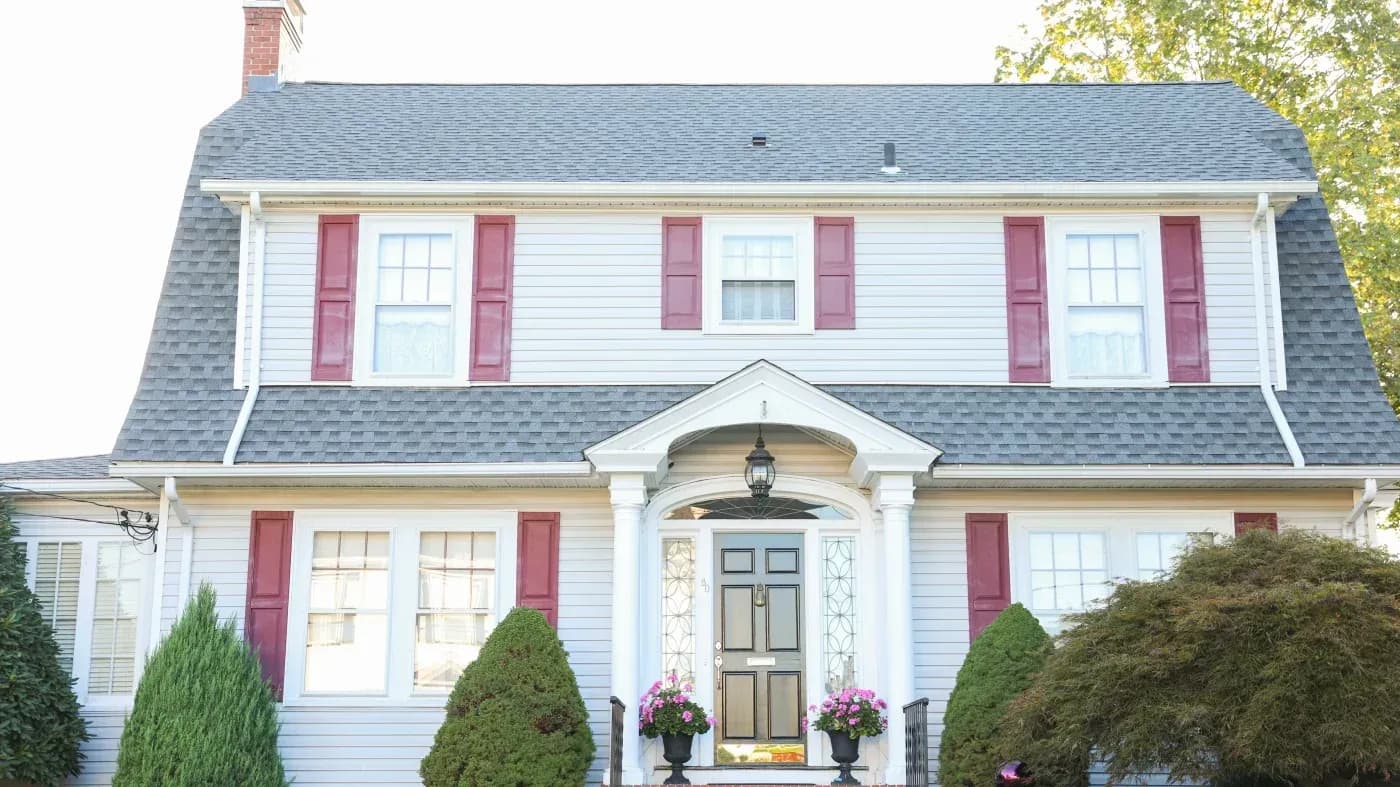 Front view of a white two-story home with red shutters, a gray shingle roof, and a columned entryway.