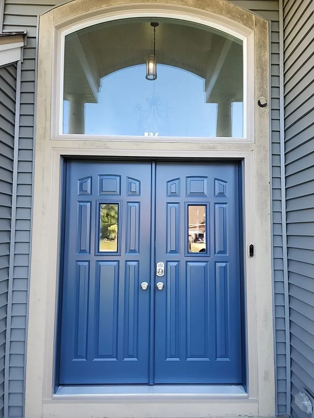 Blue double entry doors with glass panels, transom window, and pendant light in arched stone entryway