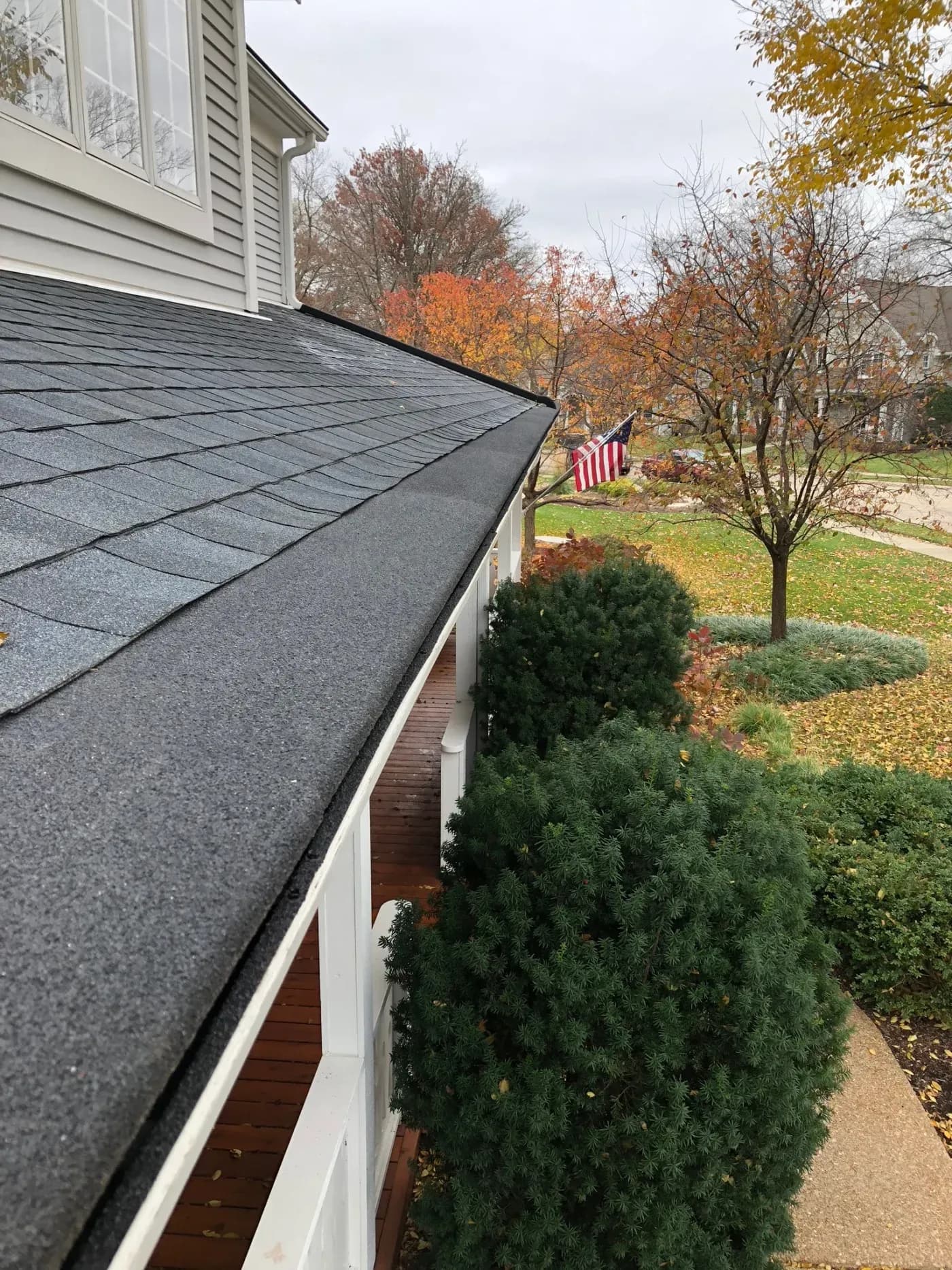 House roof and gutter with autumn landscape, evergreen shrubs, and American flag in residential yard