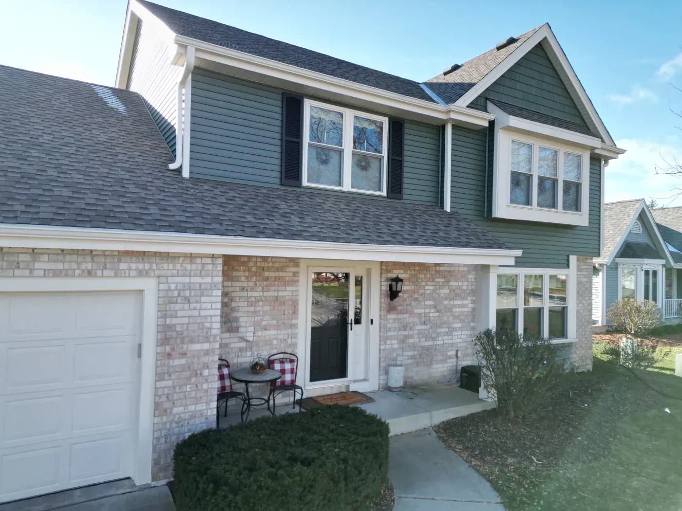Two-story suburban home with brick and siding exterior, two-car garage, front patio with seating, and dormer windows on the upper level