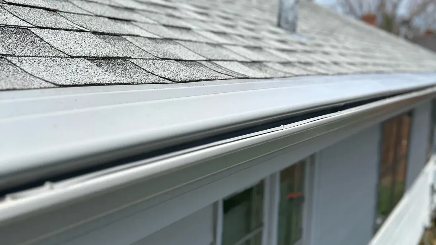 Close-up of white vinyl gutter along asphalt shingle roof edge, showing proper drainage system installation