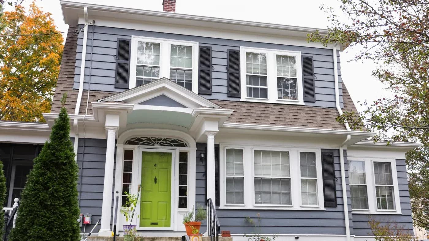 Colonial-style house with blue-gray siding, white trim, and bright lime-green front door, surrounded by autumn foliage