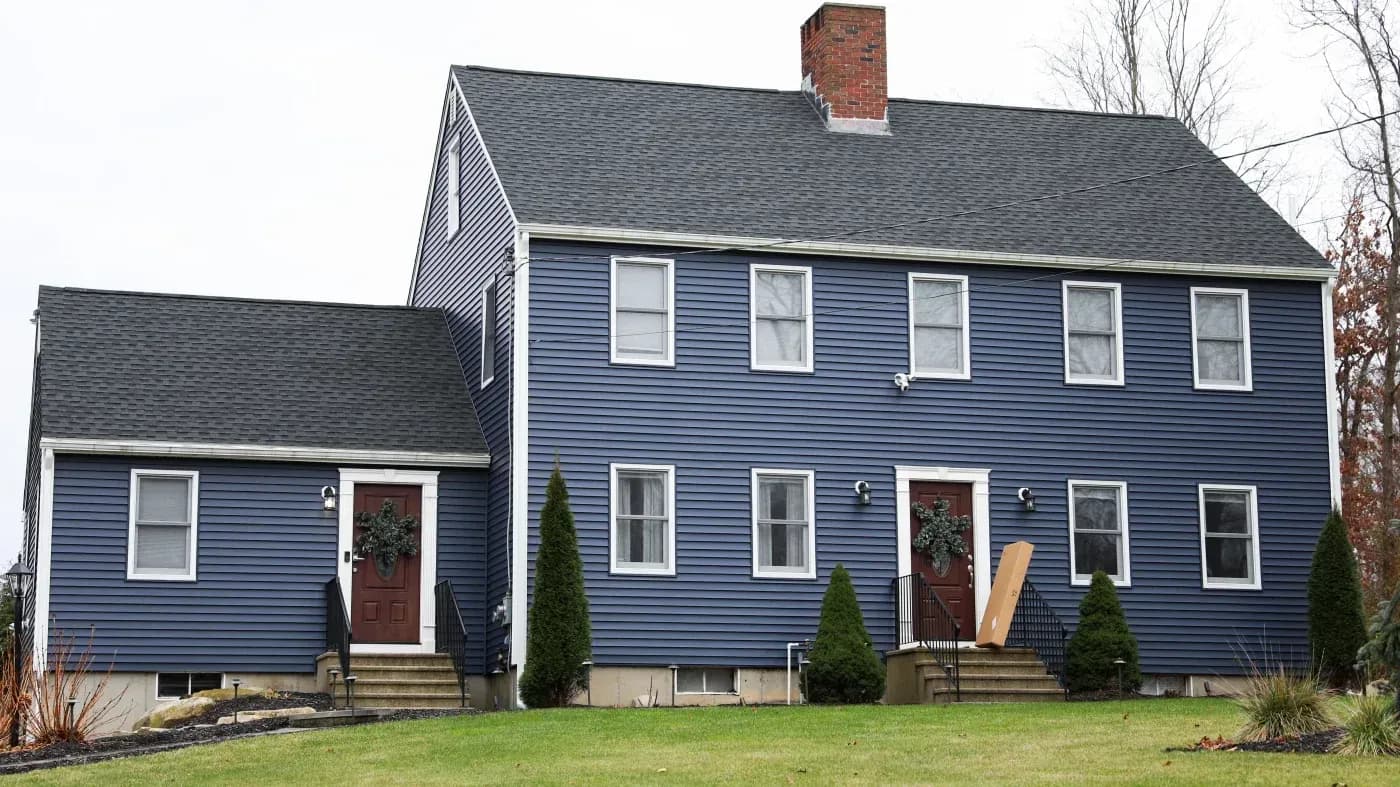 Blue two-story home with white trim, dark asphalt shingle roofing, and two front entrances.