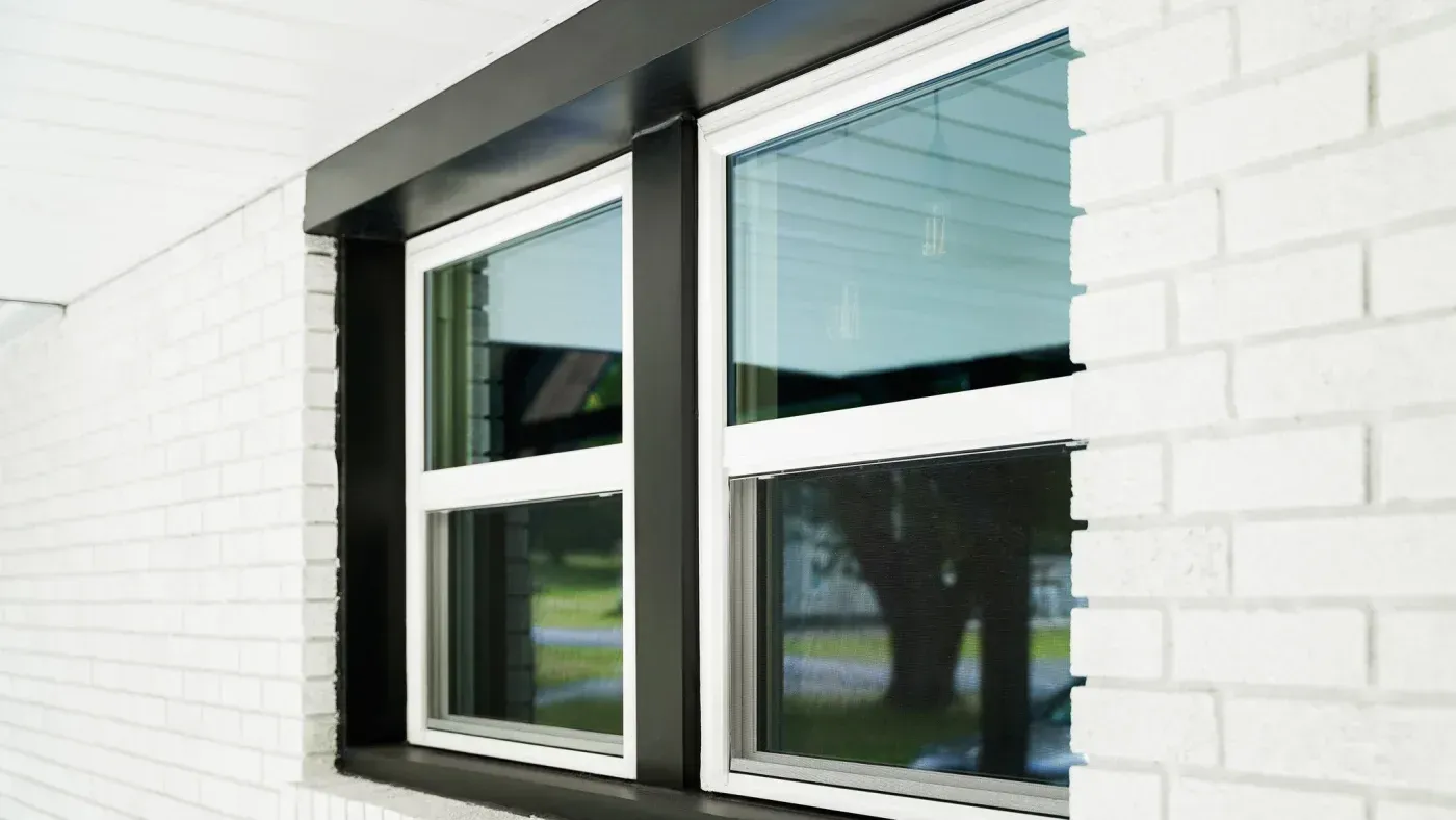 Modern black-framed casement windows with white brick surround, featuring operable panes and integrated blinds, installed on residential exterior wall