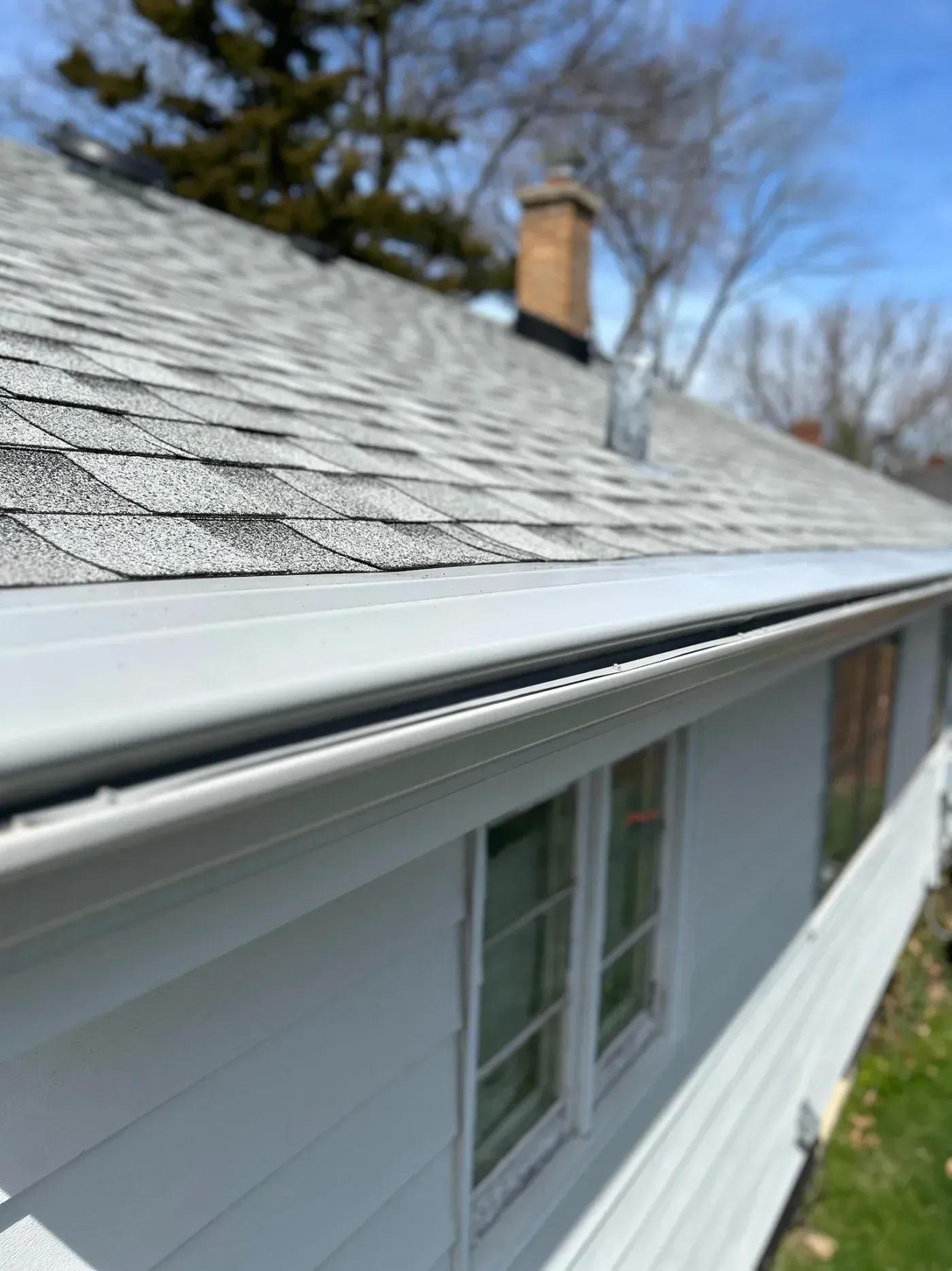 Close-up view of a residential gutter system along a roof with asphalt shingles and chimney visible in background