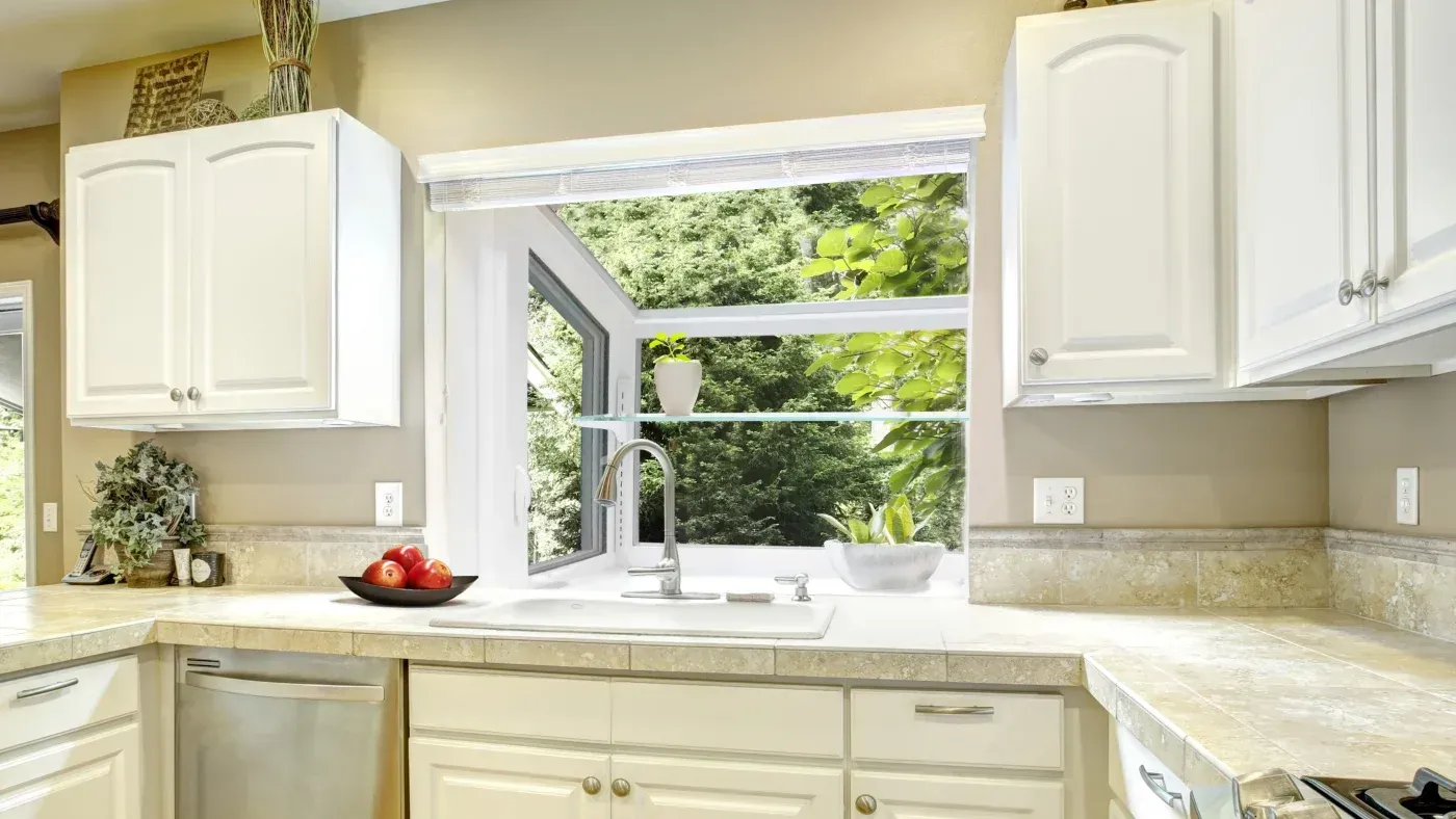 Bright kitchen with white cabinetry and granite countertops, featuring a large window overlooking green foliage and a sink with gooseneck faucet