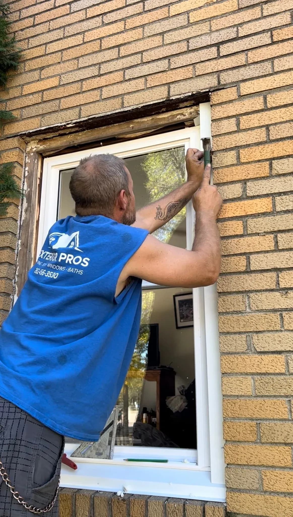 Professional window installer in blue shirt adjusting window frame on brick building with damaged lintel above