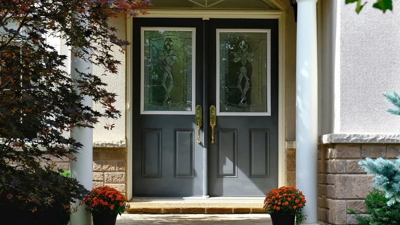 Black double doors with decorative glass panels flanked by red chrysanthemums on an entryway with stone and stucco facade