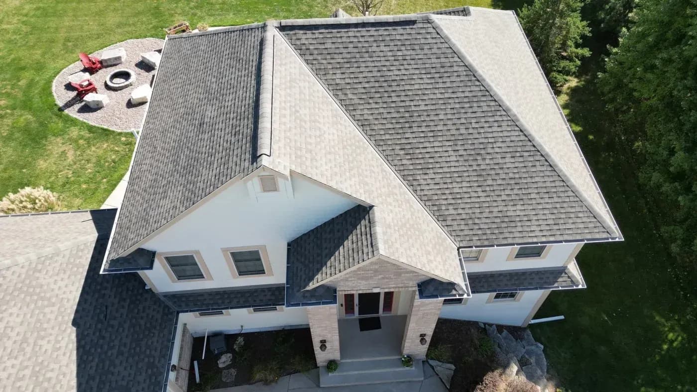Overhead drone view of a large home with intersecting gray shingle rooflines and a covered front entrance.