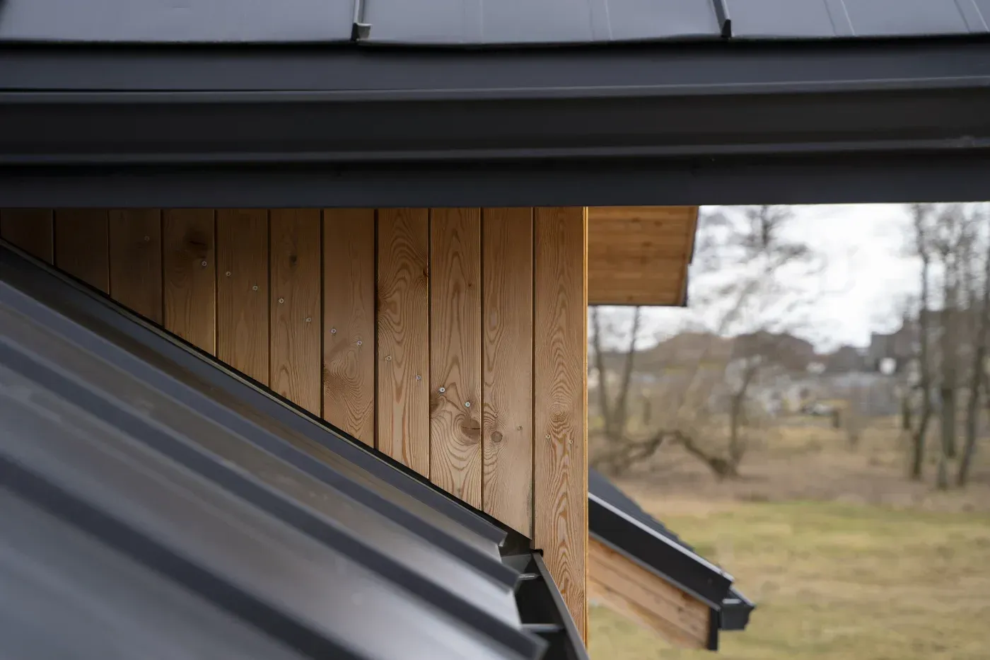 Close-up of black metal roofing, matching gutters, and vertical natural wood siding.