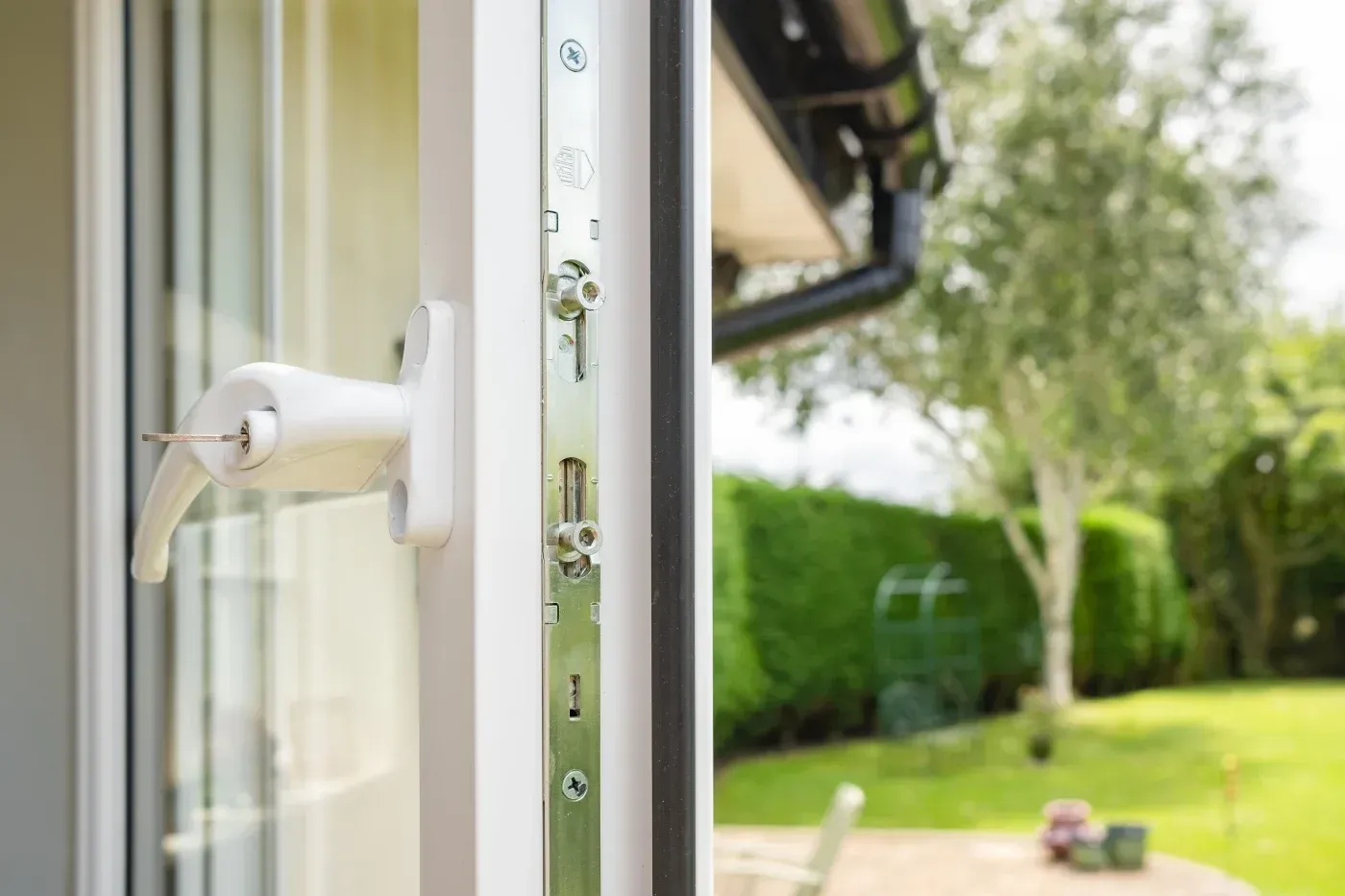 Close-up of a white replacement window handle and locking hardware with a backyard view in Ashippun, Wisconsin.