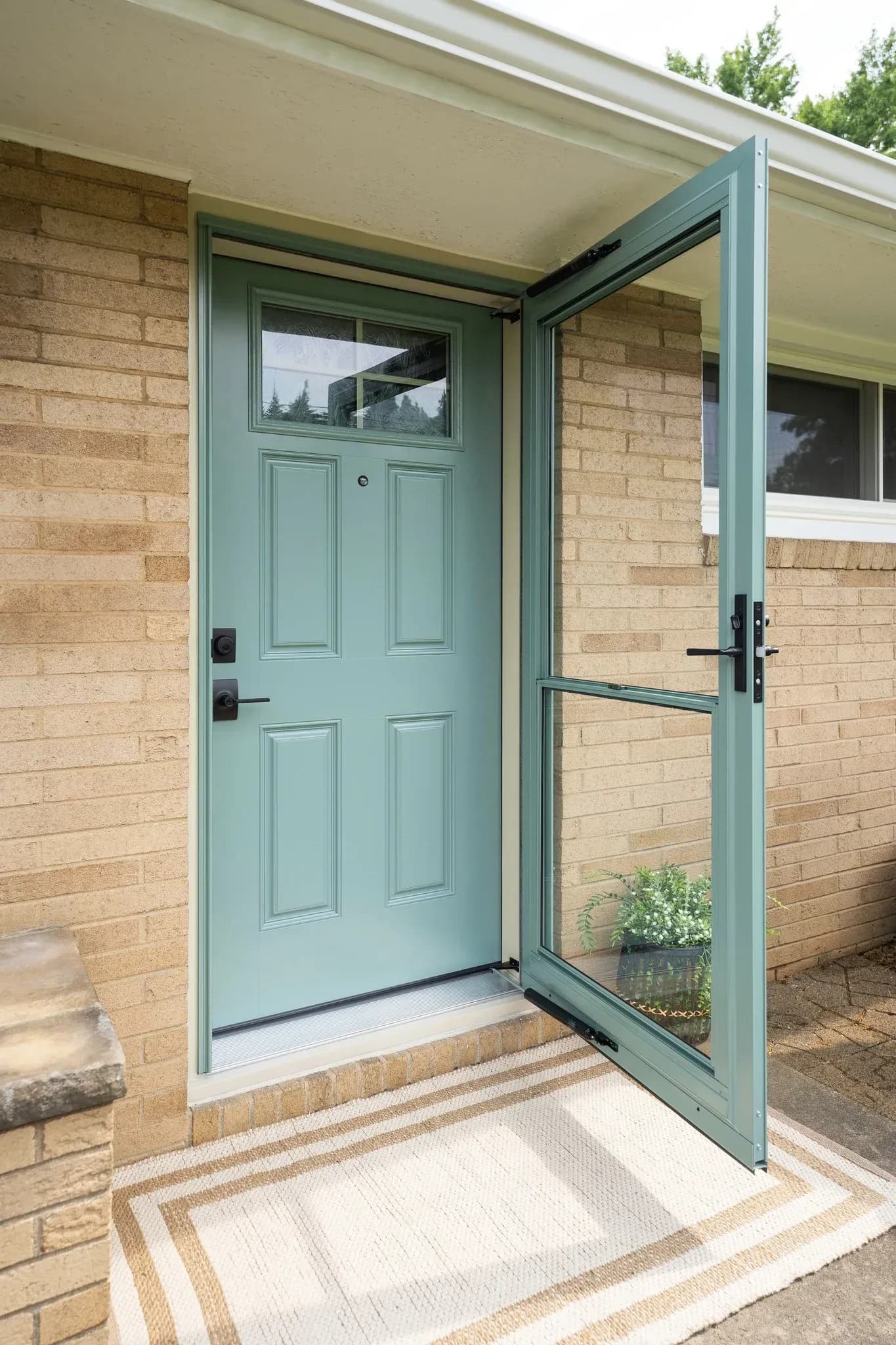 Modern front entry with light green paneled door and matching glass storm door, brick exterior, and covered porch