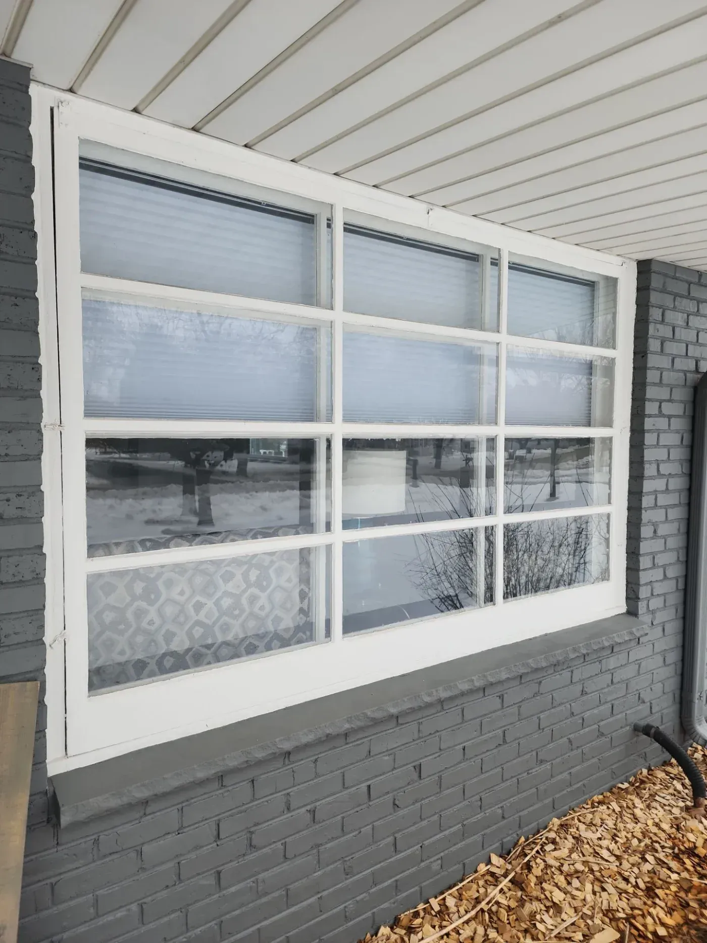 White aluminum garage door with 12 glass panels and horizontal stripes, mounted on gray brick wall under polycarbonate roof