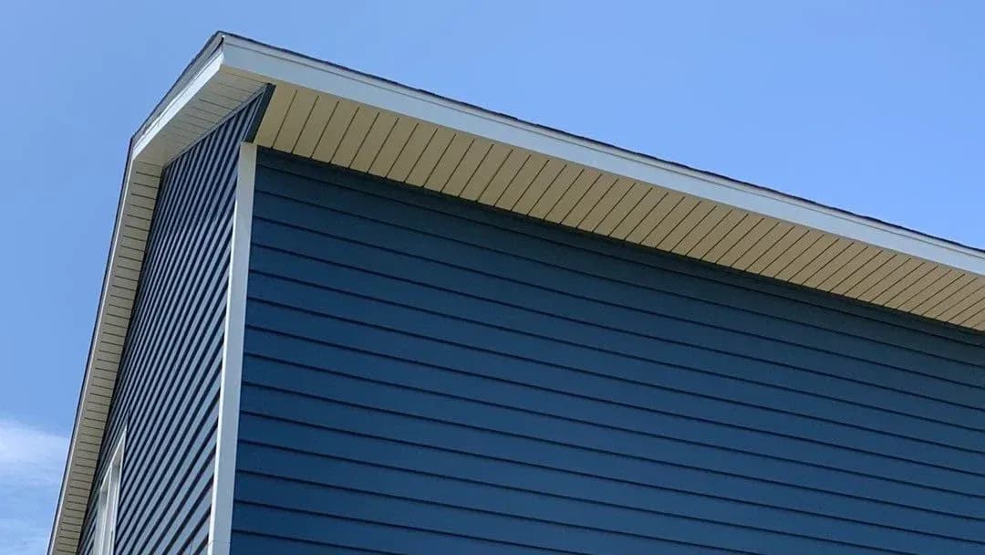 Modern building corner with dark blue horizontal siding and tan metal roof against clear blue sky