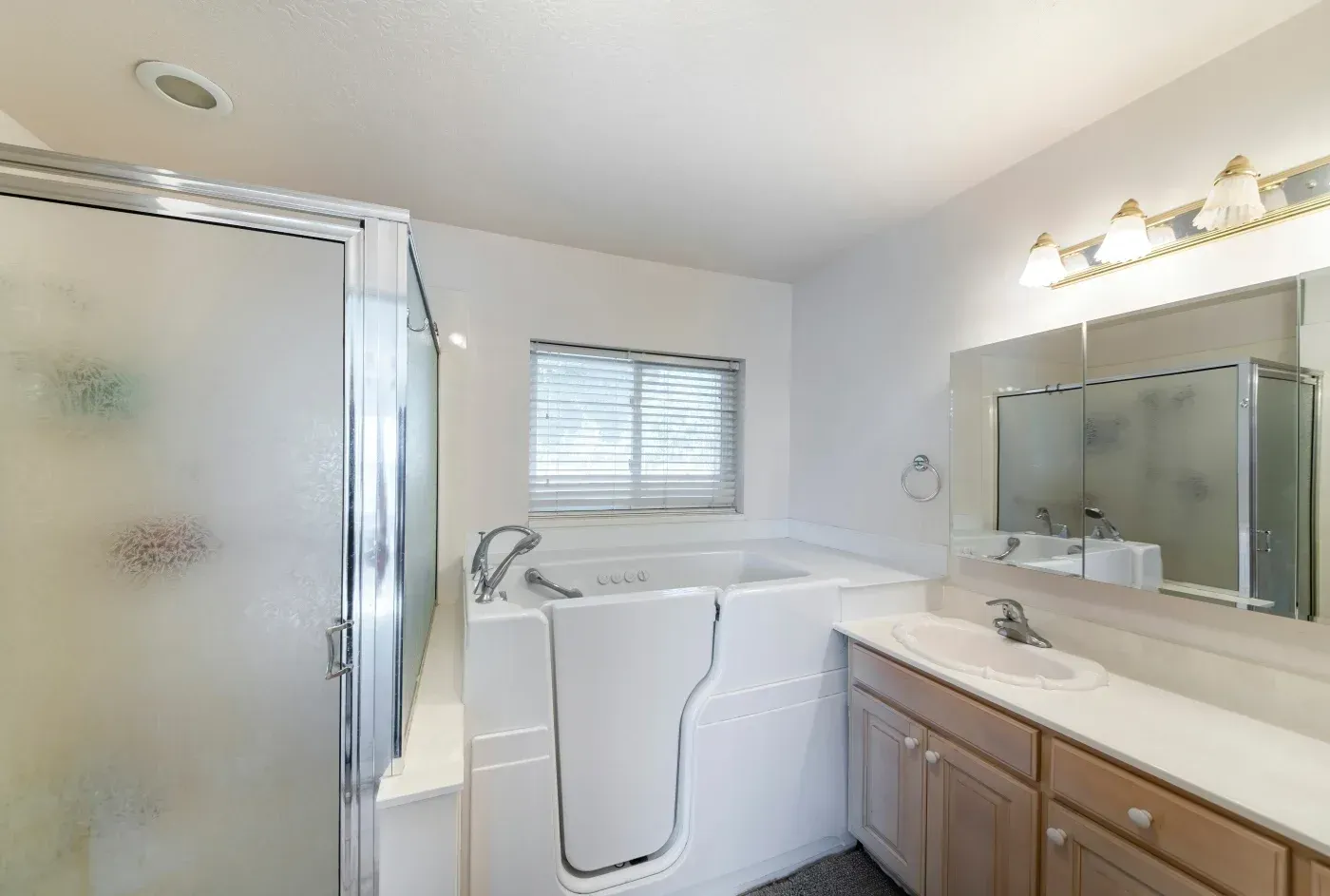 Accessible white walk-in tub beside a glass shower and wooden bathroom vanity.