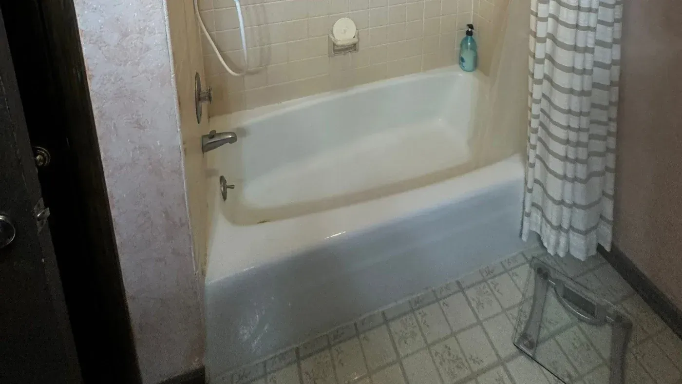 Bathroom with white bathtub, beige tile surround, striped shower curtain, and bathroom essentials on shelf and tub edge