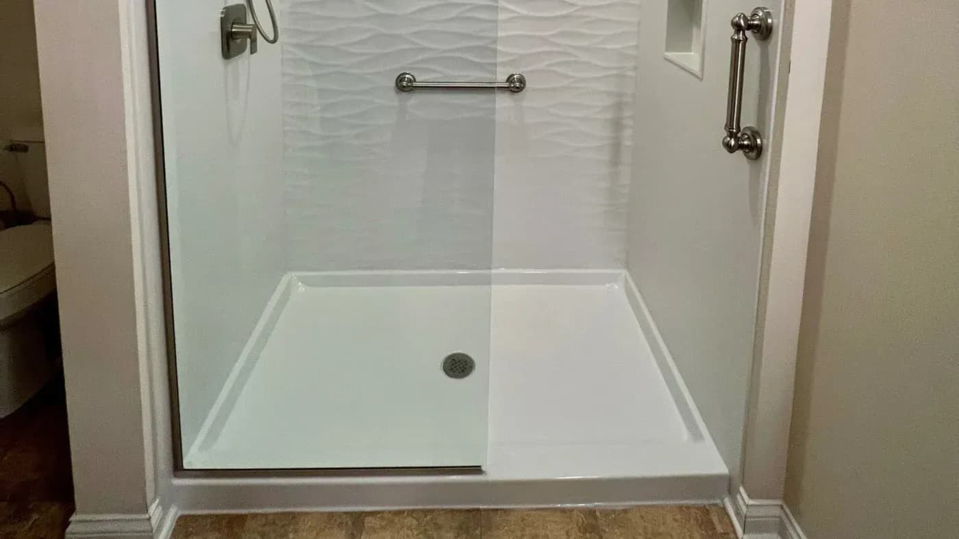 Modern walk-in shower enclosure with textured white tile walls, glass sliding door panels, chrome grab bars and rainfall showerhead, and white base pan with centered drain