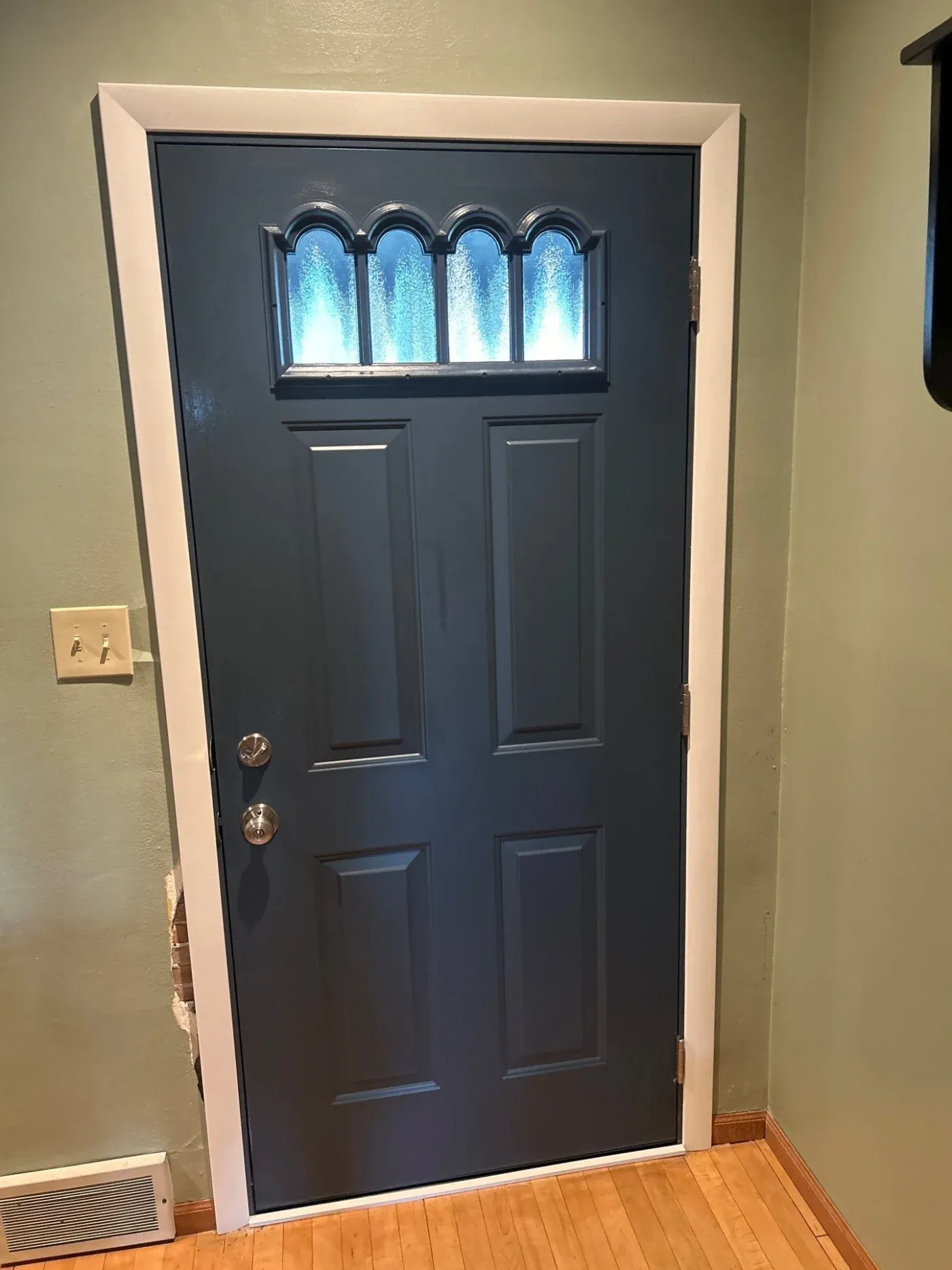 Navy blue entry door with arched transom window featuring four panes with frosted glass, brass knobs, and white trim frame