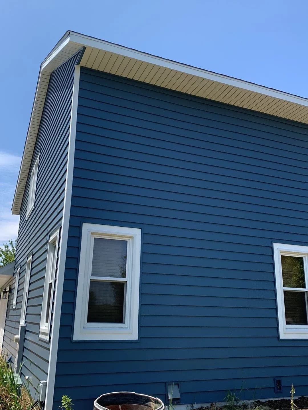 Modern blue house exterior with white-trimmed windows and horizontal siding, featuring a tan metal roof overhang and vertical corrugated siding accent on the corner