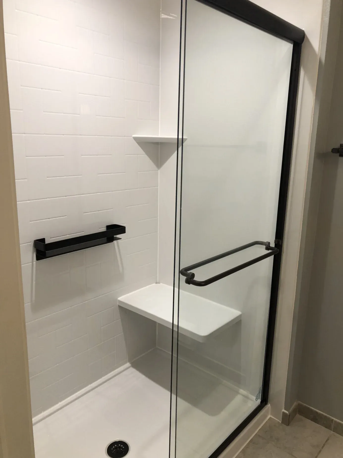 Modern bathroom shower with white subway tile walls, glass enclosure with black frame, built-in bench seat, and black towel bar and grab handles