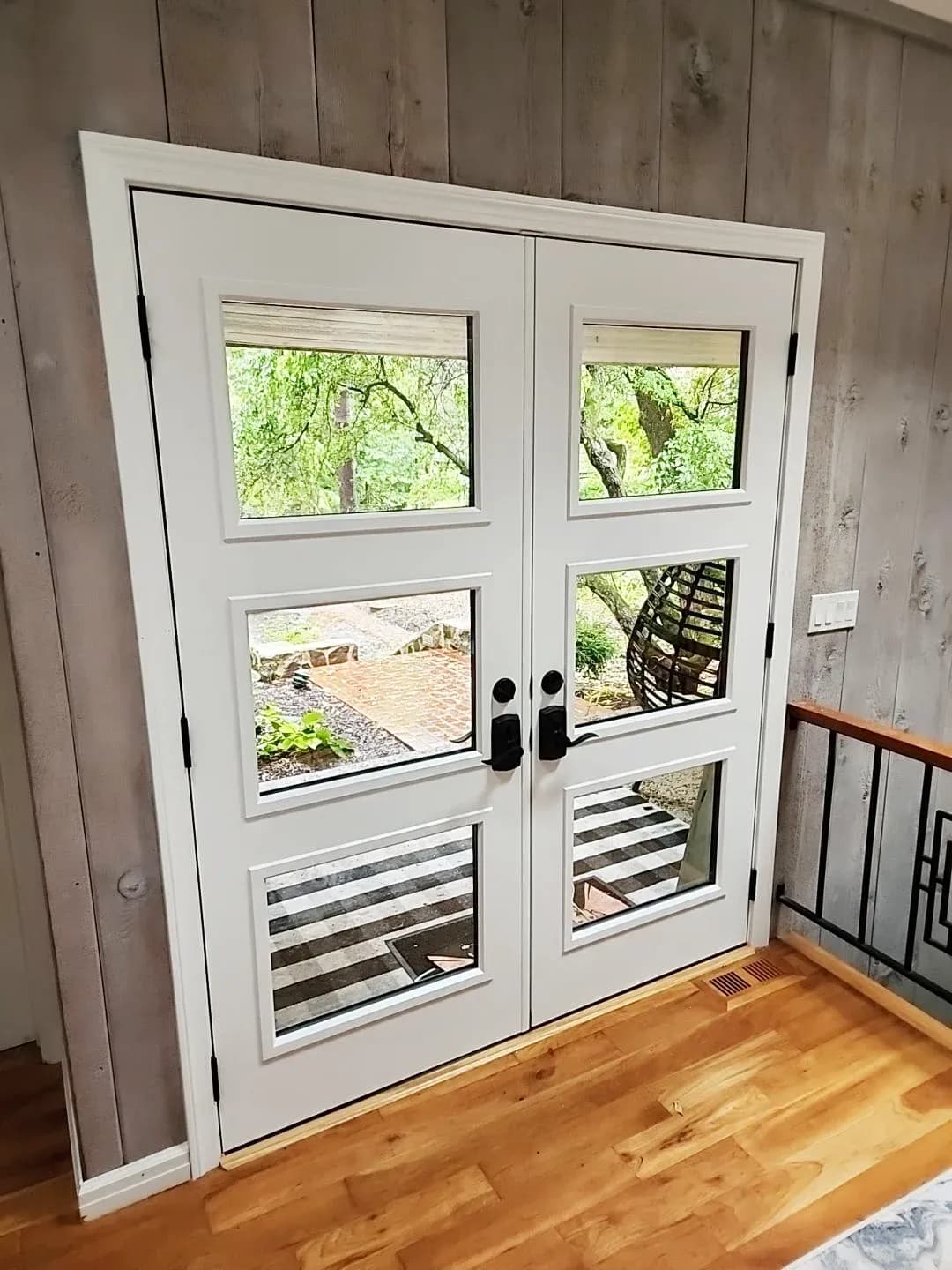 Pair of white French doors with multiple glass panes opening to a backyard patio and landscaping with trees