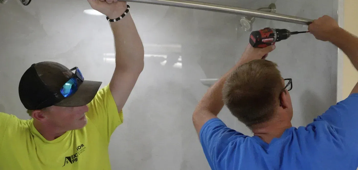 Two workers in safety gear drilling into a drywall ceiling with a power drill during interior construction work