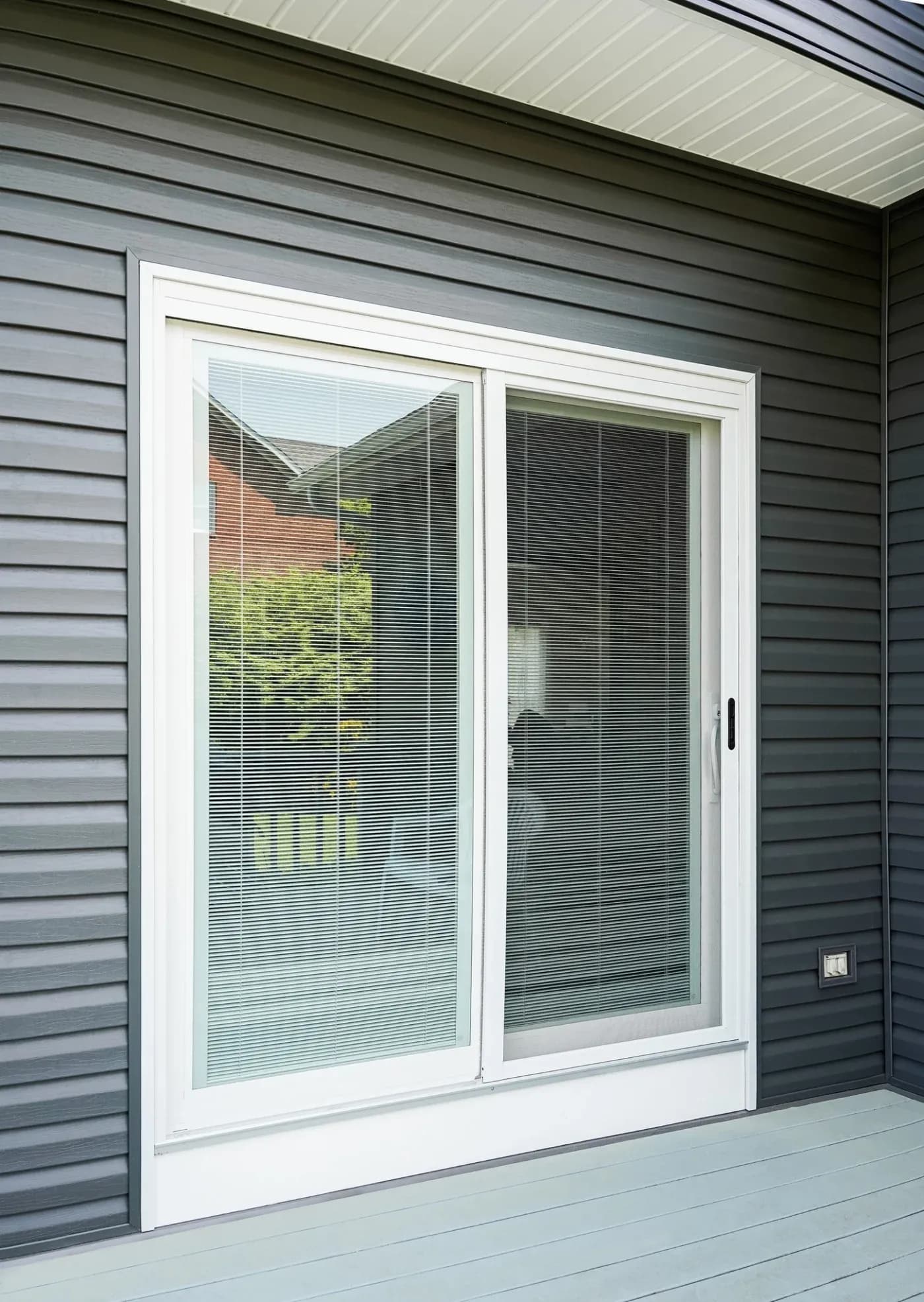 White frame sliding glass doors with integrated blinds on gray horizontal siding exterior wall