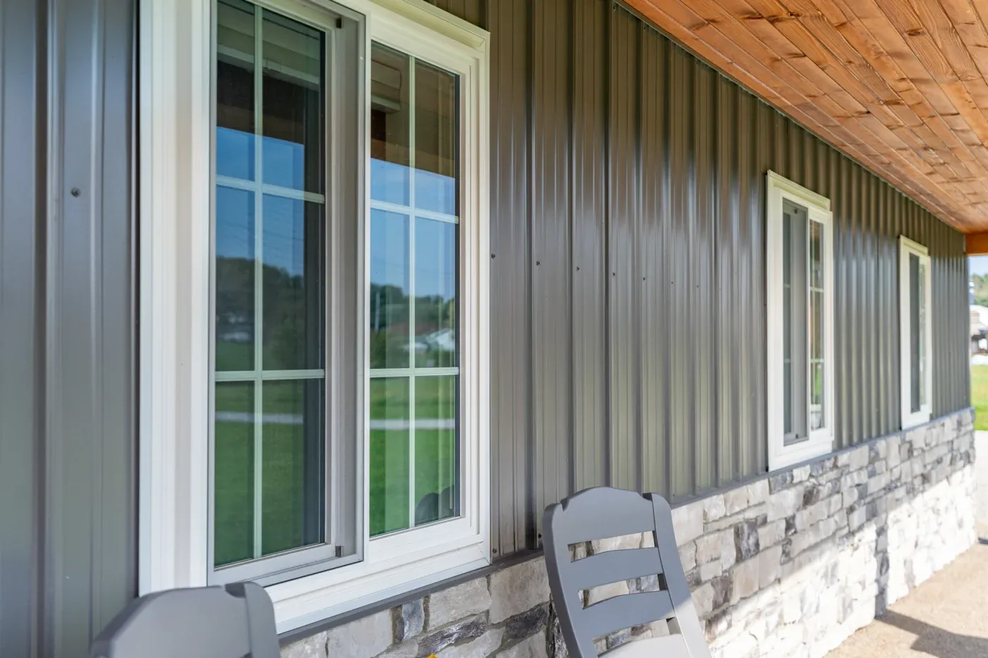 Modern farm building exterior with white-trimmed windows and doors on corrugated metal siding, stone foundation, wooden ceiling, and outdoor seating area