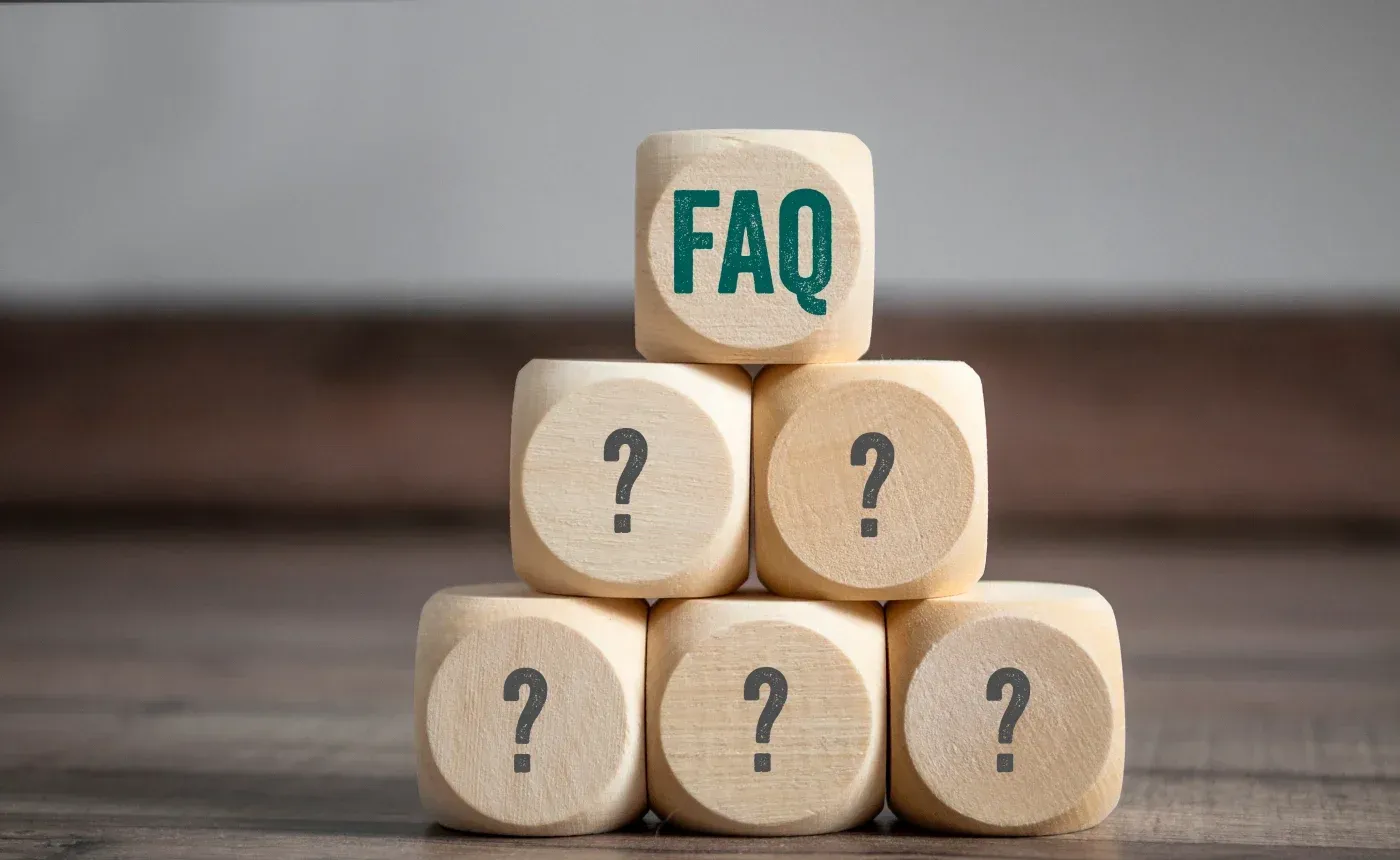 Wooden blocks stacked in a pyramid with FAQ text on top block and question marks on the five blocks below, representing frequently asked questions