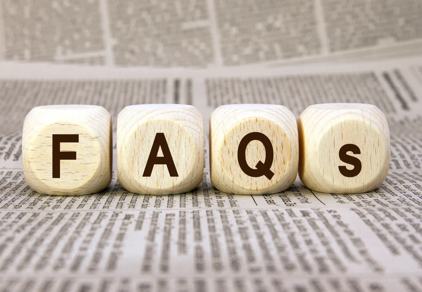 Four wooden blocks spelling FAQS on top of printed document pages