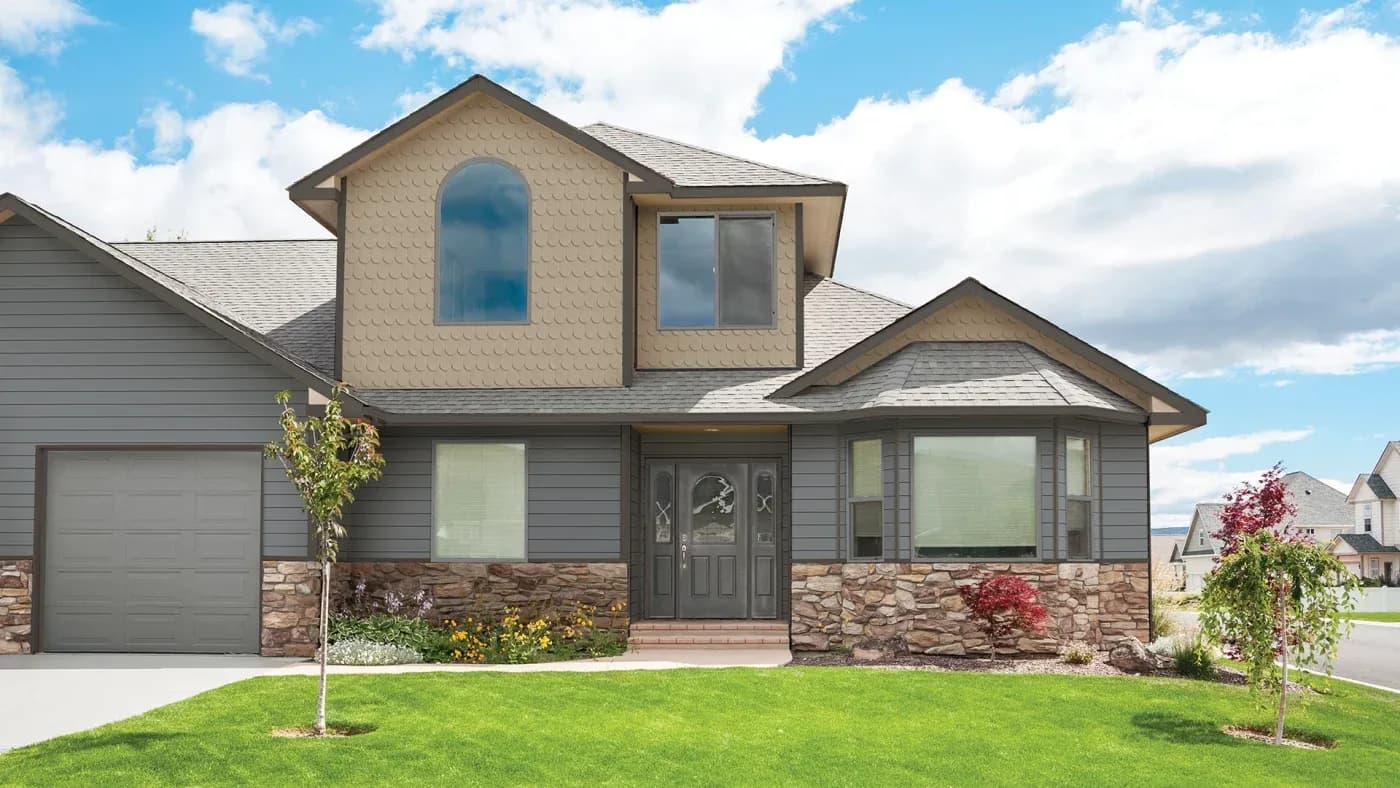 Two-story suburban home with stone and siding exterior, two-car garage, arched upper windows, and landscaped front yard with young trees