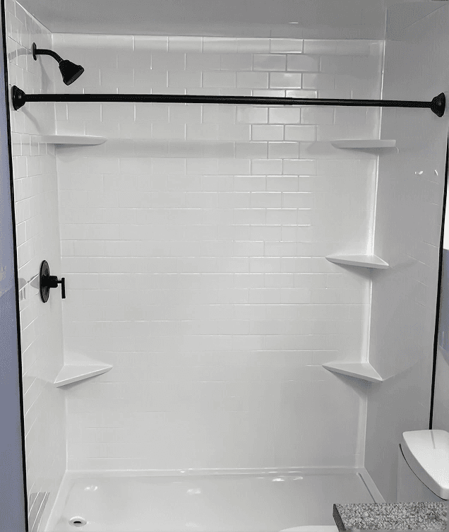 Modern bathroom shower enclosure with white subway tile walls, black framed glass door and showerhead, built-in shelving, and white bathtub edge visible