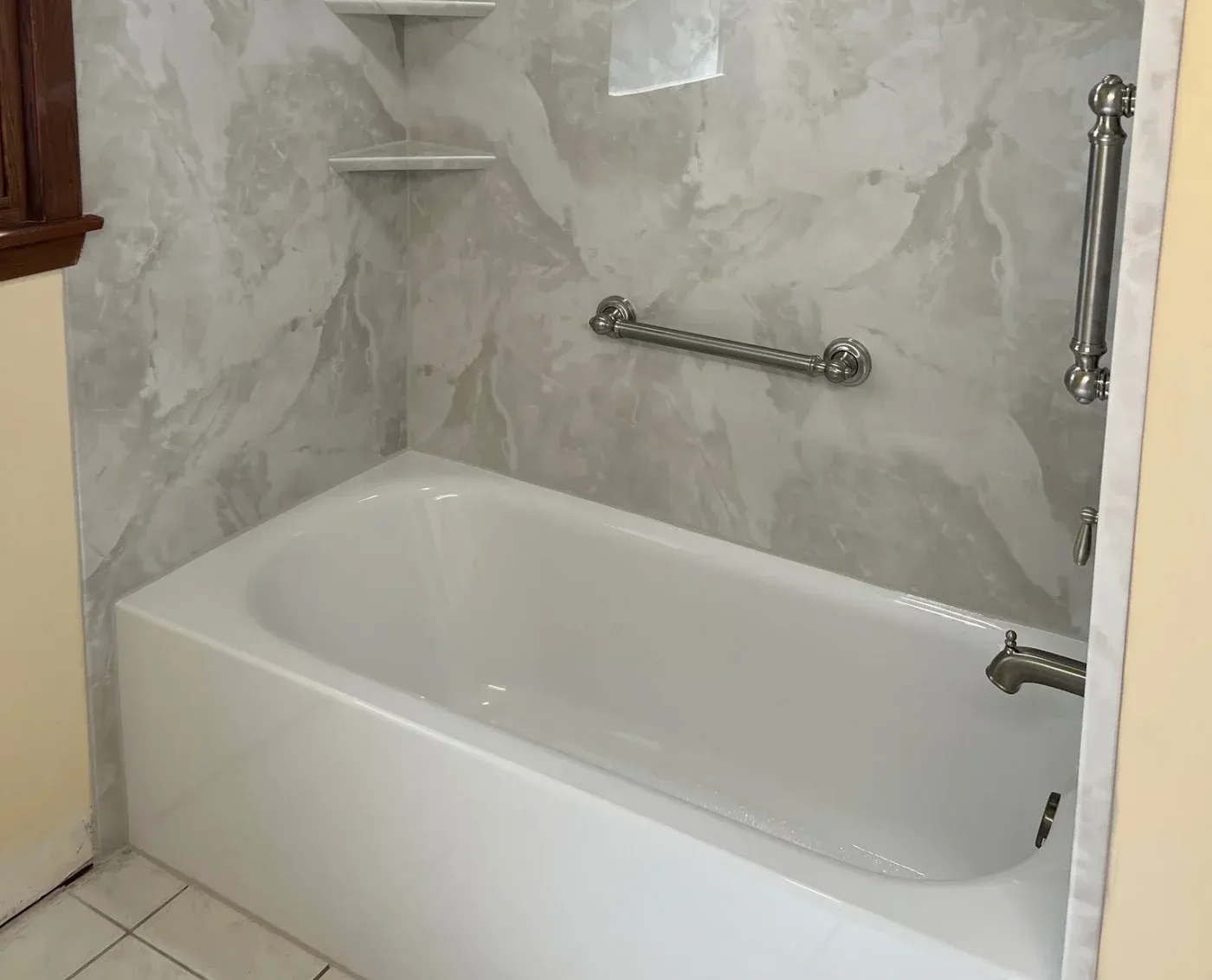 Modern bathtub with white acrylic surround, marble-look wall panels, chrome grab bar and towel rack, and chrome tub spout