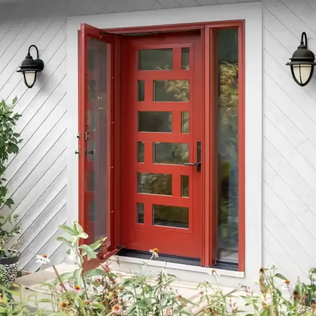 Red modern front door with horizontal glass panels and sidelights, flanked by black wall sconces on white siding